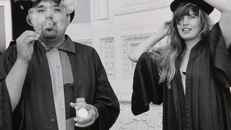 Two students in tams and gowns blow bubbles at the camera.