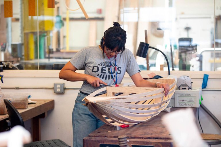 Photo of Balqis Indriyani working over the wood frame of a boat-shaped object.