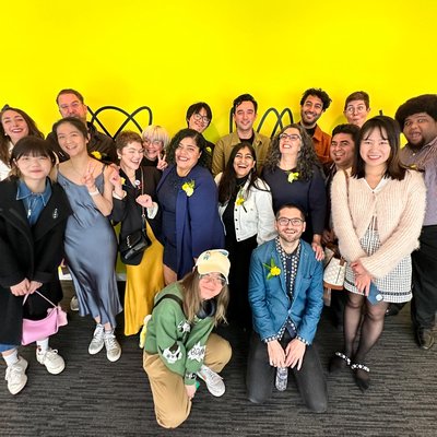 A group photo of students and faculty in front of a yellow wall.