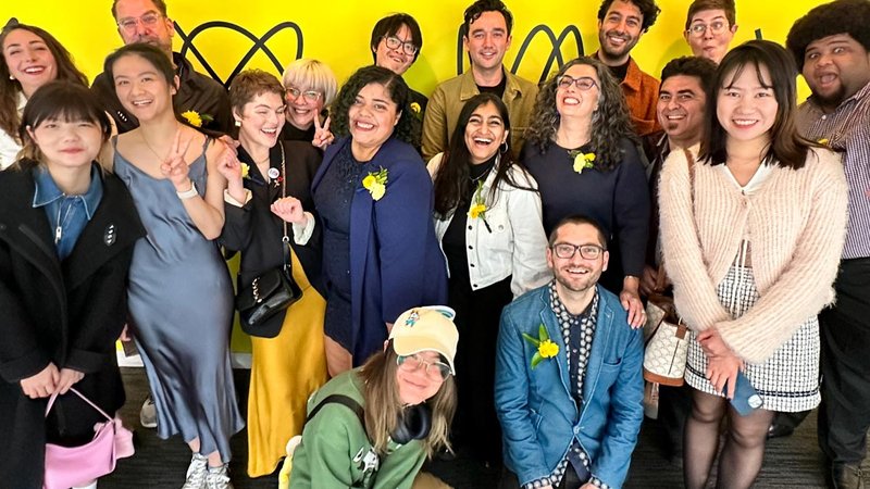 A group photo of students and faculty in front of a yellow wall.