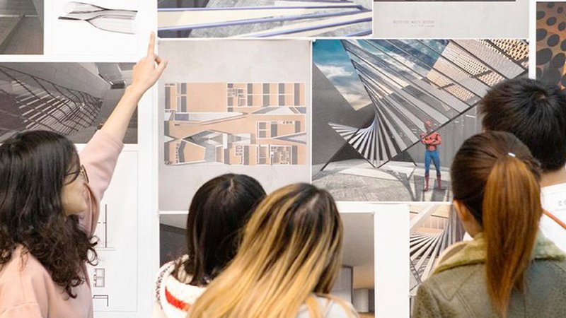 One student points up at a wall of Architectural illustrations, three students look on.