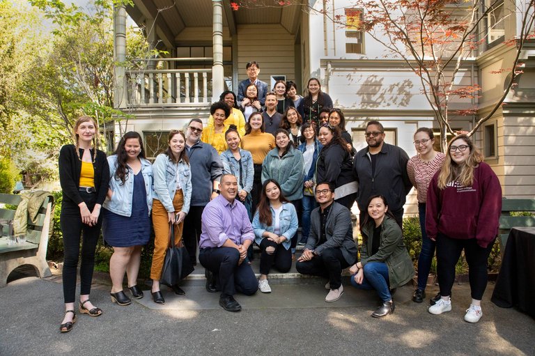A diverse group of people pose together for a photo in front of an old house.