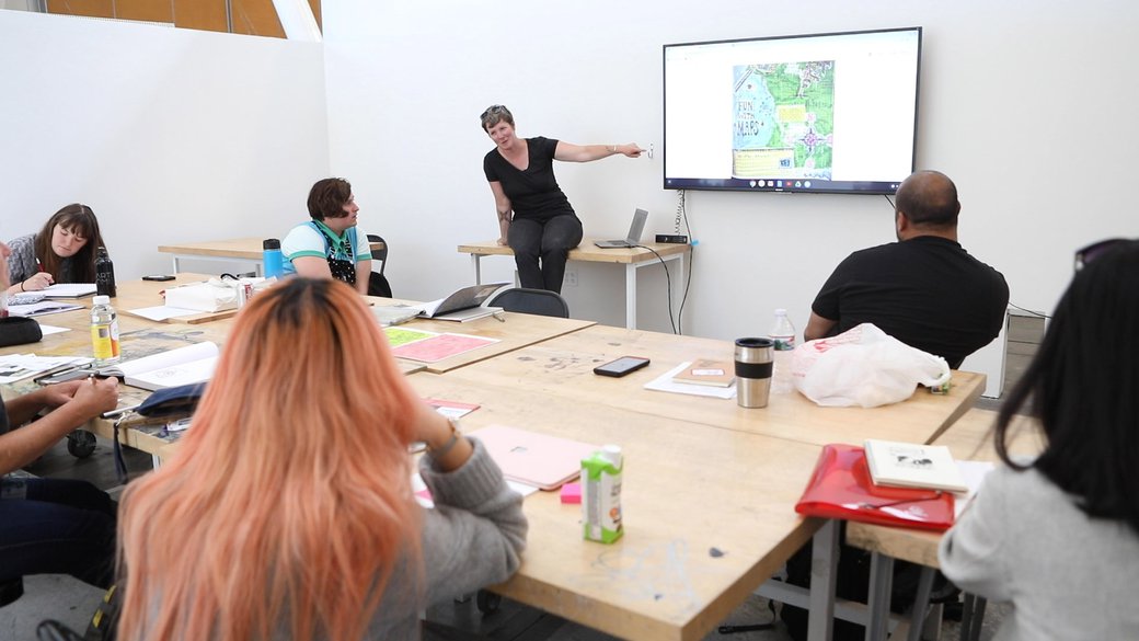 A professor points to a comic on screen in a classroom with Comics program students.