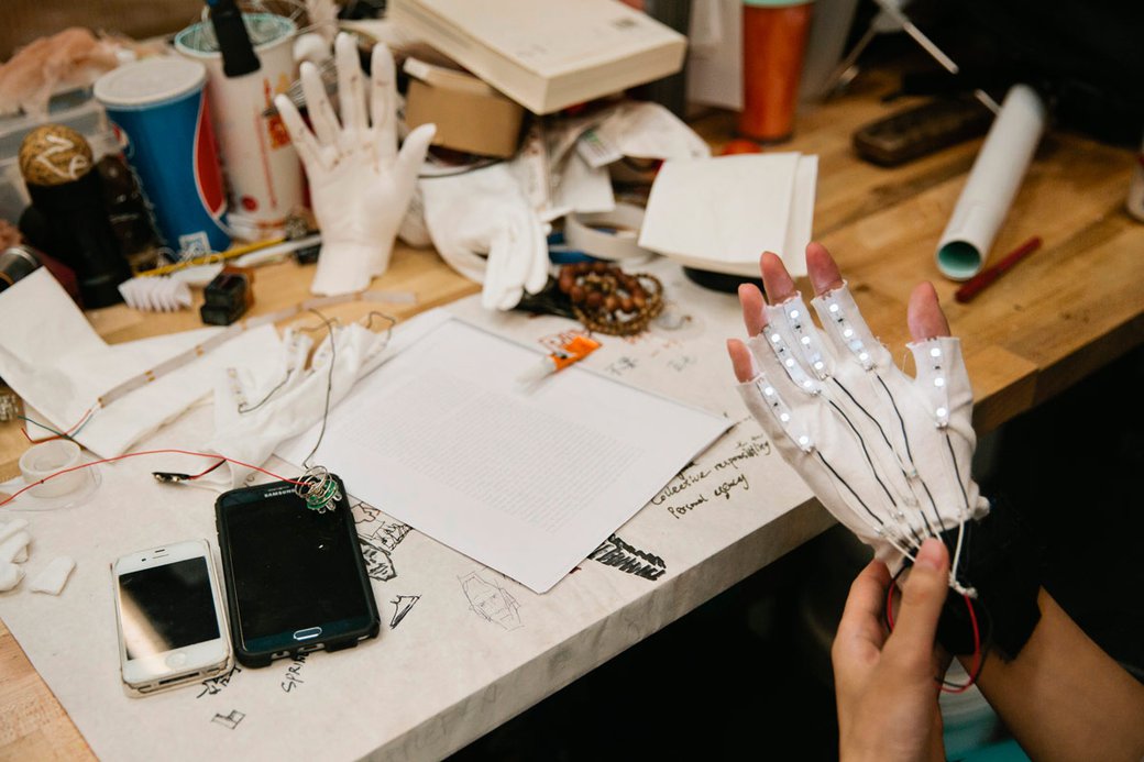 A person looks at their gloved hand with cords and sensors attached.
