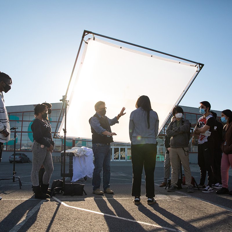 Film class learning about lighting techniques from their professor on the back lot.