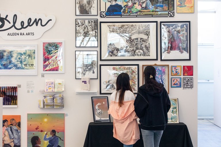 Two people look up at a couple illustration student work at the end of year show.
