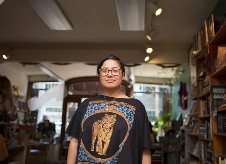 Dorothy Santos stands in the middle of a book shop with an archway above them, looking directly into the camera.