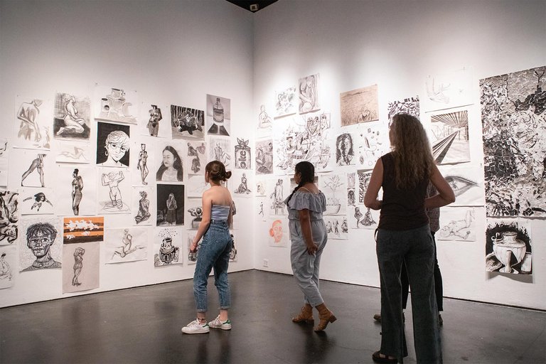 Students walk through an exhibition of drawings.