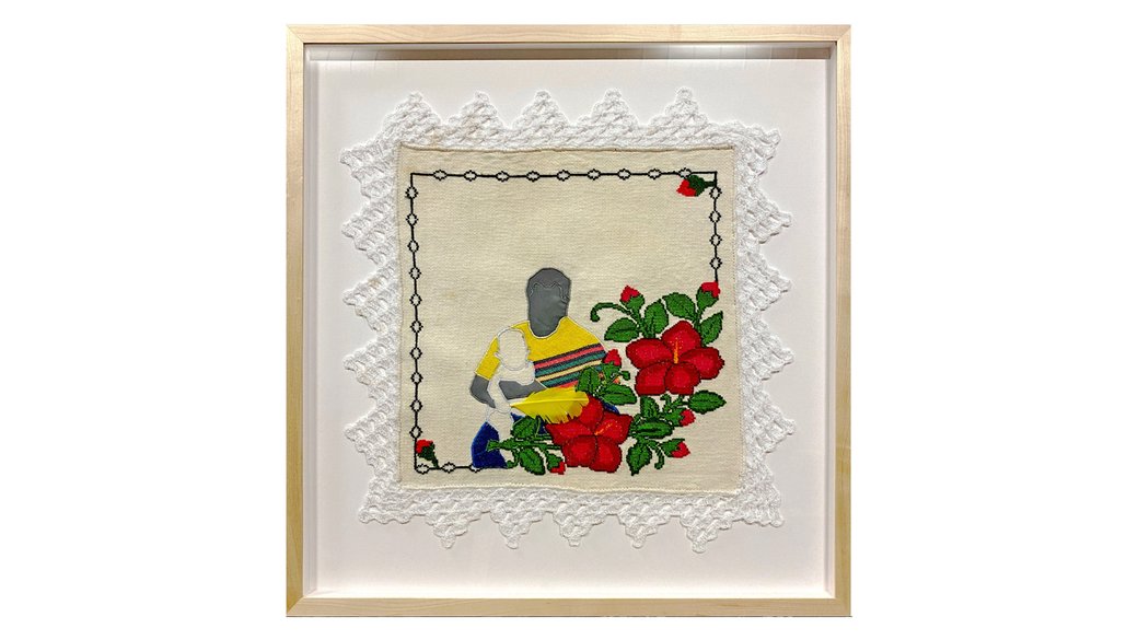 A framed embroidery of a mother with a child on her lap; their faces are silhouetted. Roses border the image.