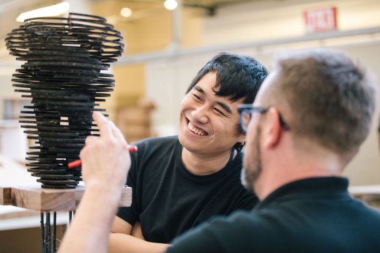 An architecture student smiles as a professor points at their model.