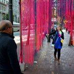 a woman walks through thousands of dangling neon strings on the street in San Francisco.