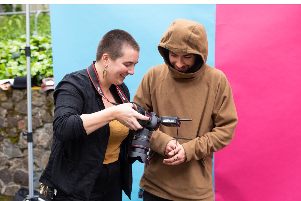 A studio manager smiles as she shows a student his portrait on the camera's LCD screen.