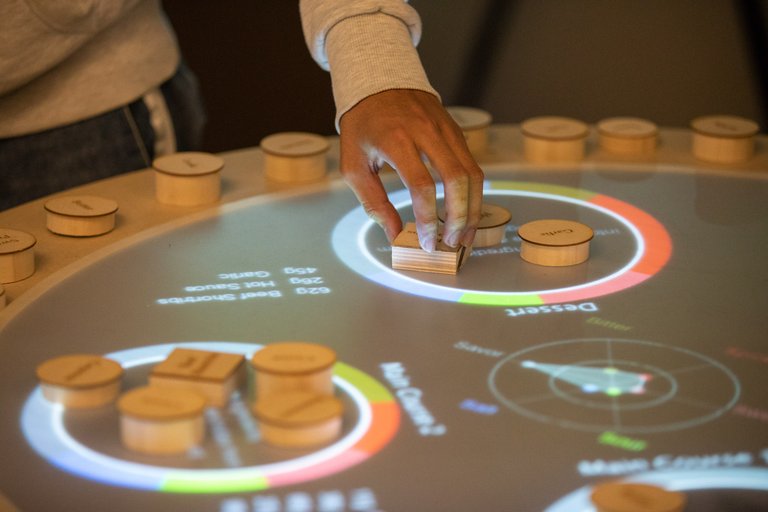 A close-up photo of a hand moving game pieces over a digital board illuminated from below.