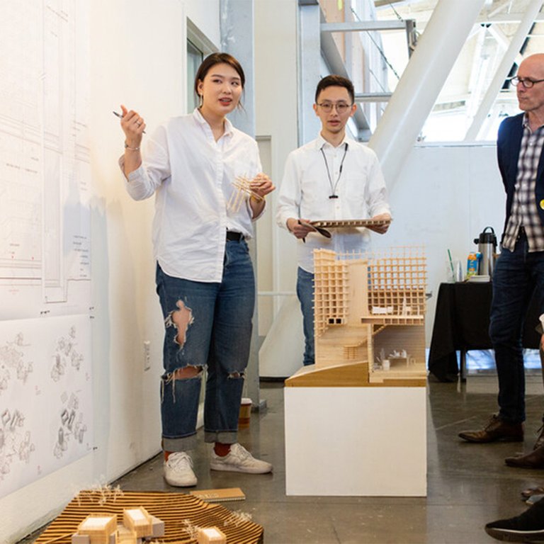 Two CCA architecture students present their work in both drawings and model form during a critique.