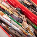 A close-up view of colorful brushes and palette knives in a red toolbox.