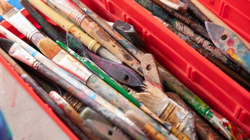 A close-up view of colorful brushes and palette knives in a red toolbox.