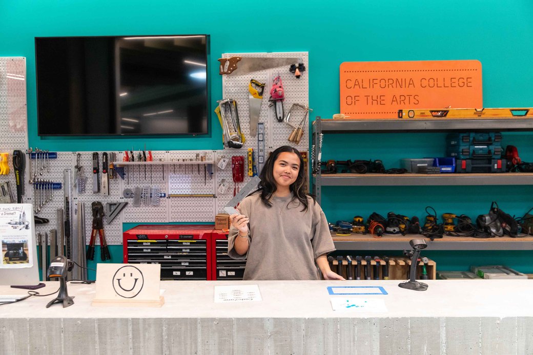 A student stands smiling behind a concrete desk amid a blue-green backdrop