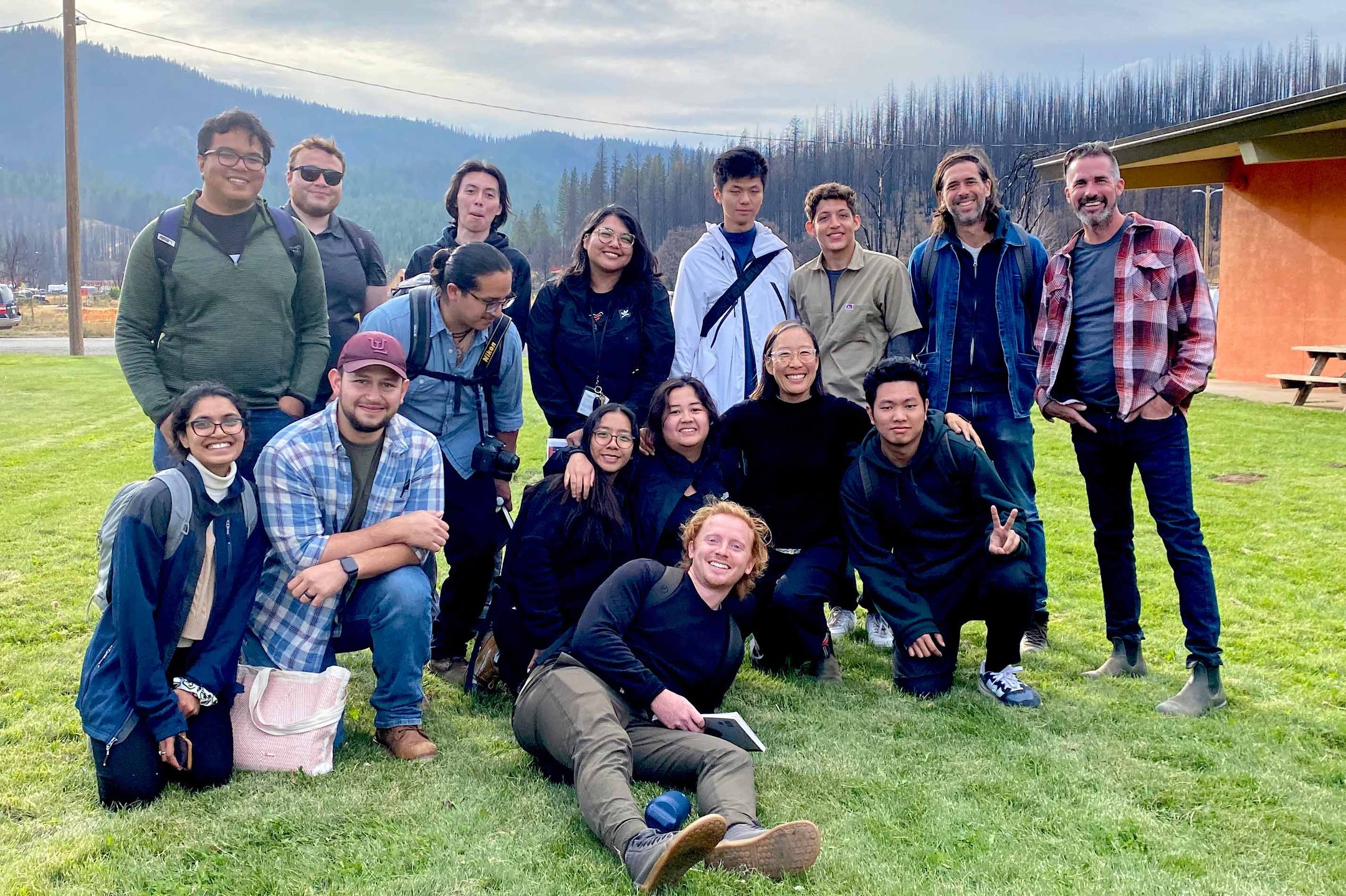A group portrait of over a dozen people affiliated with CCA Architecture posing with a forest in the background.