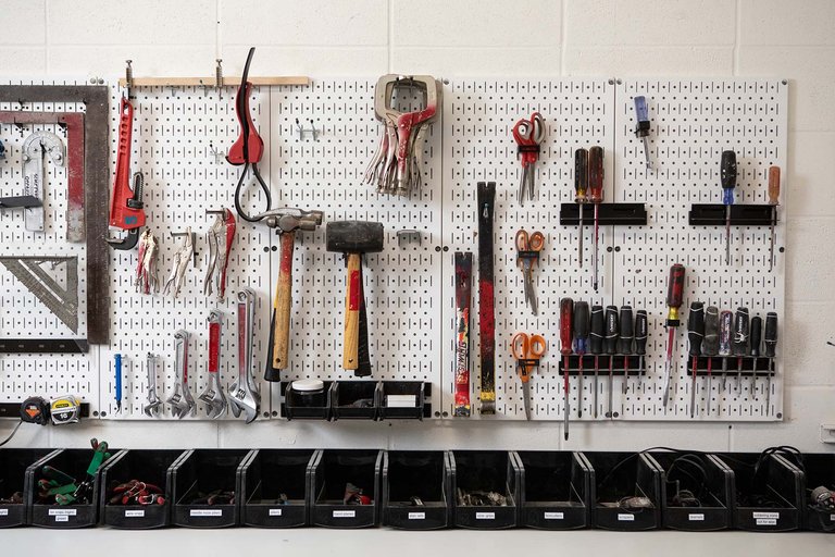 Various woodshop tools, like clamps and hammers, organized on white pegboard.