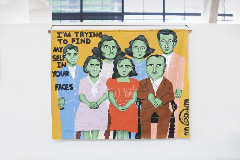 A painting of figures with text, “I’m trying to find myself in your faces.”