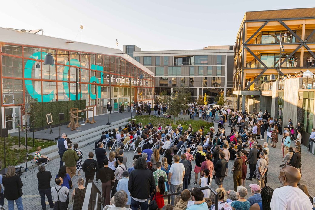 A diverse crowd of people gathers outside a building, chatting and enjoying the atmosphere together