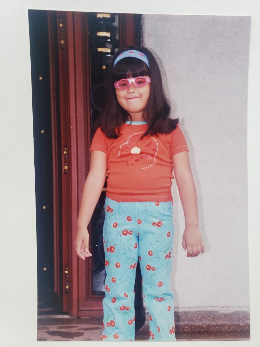 Melissa Rodriguez as a little girl, with bright patterned pants and pink statement sunglasses.