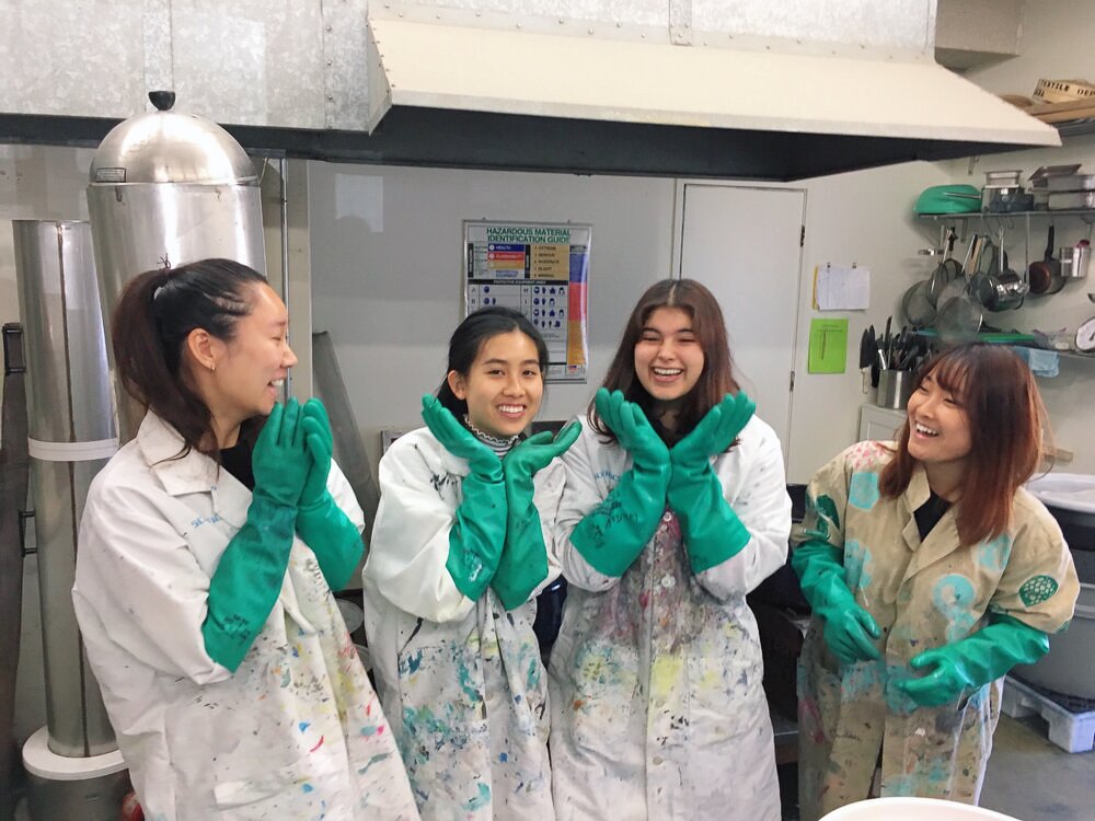 Four students smile and pose in white lab coats and teal industrial gloves.