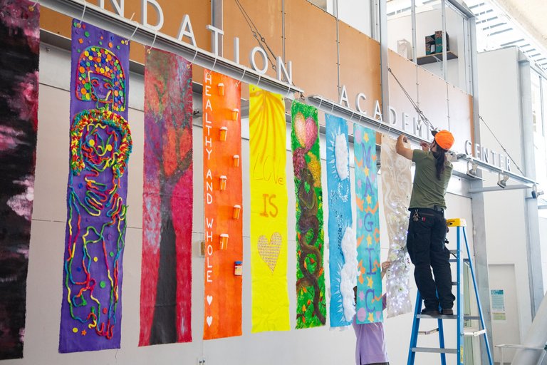 A photo of nine vertical banners each with a different design and together forming the colors of the rainbow.