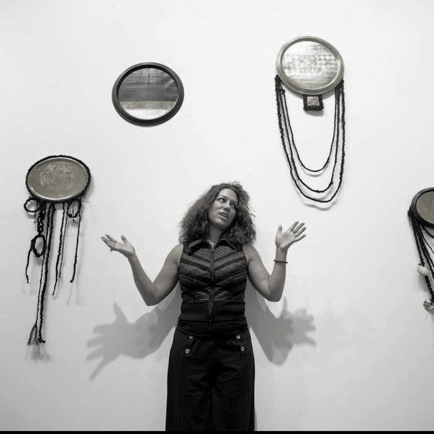A black-and-white photo of Angela Hennessy among her work with her hands outstretched