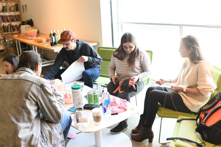 Five participants sit on green chairs around a table while they cut fabric and yarn.