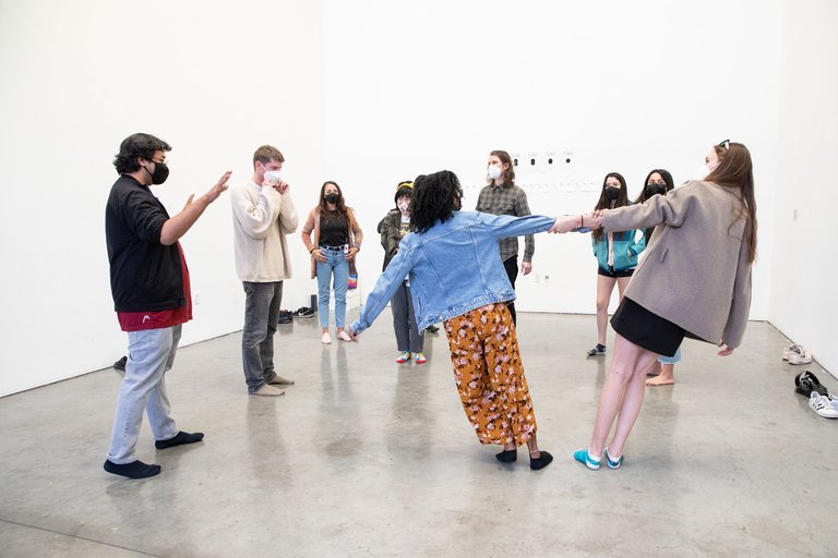 A photo of a group of students forming a semi-circle with two students holding onto each other with one hand.
