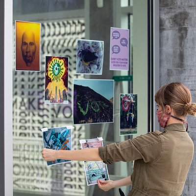 Jaime Austin holds two artworks up to the windows at the CCA Hubbell Street Galleries for the CCA@CCA artwork campaign.