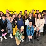 A group photo of students and faculty in front of a yellow wall.