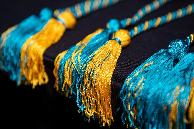 Three sets of golden and teal graduation tassels shine in the sun