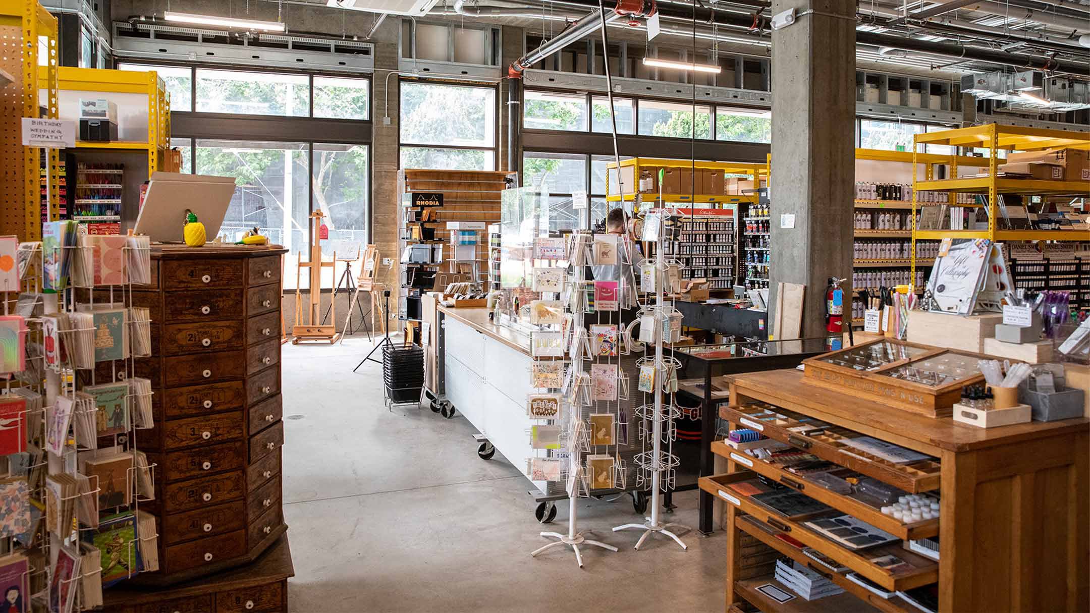 The interior of an art-supply store showing aisles of colorful paints, cards, and drawing materials.