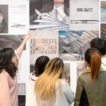 One student points up at a wall of Architectural illustrations, three students look on.