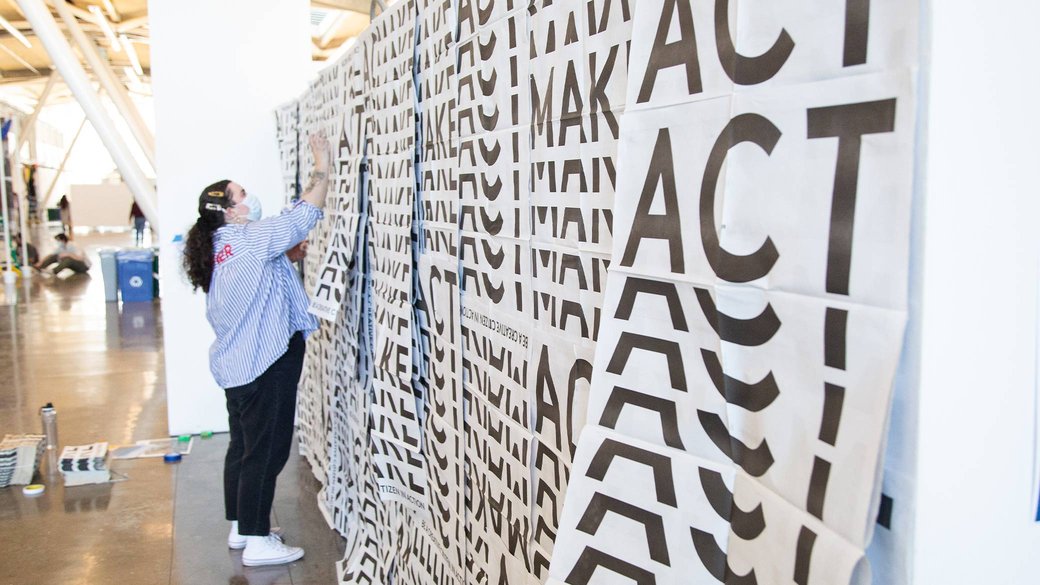 A student layers paper sheets to create a repeating installation that reads “Make. Act.”