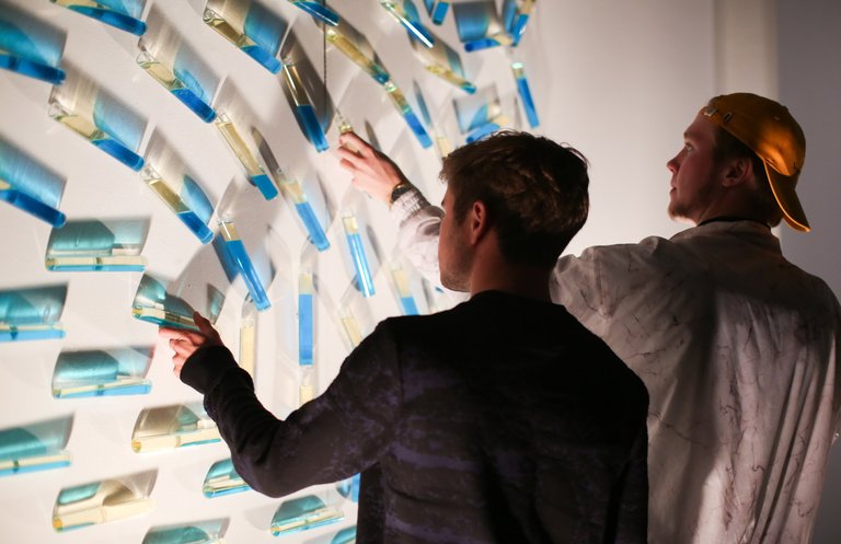 Two people engaging with fluid-filled vessels at an exhibition at Hubbell Street Galleries.