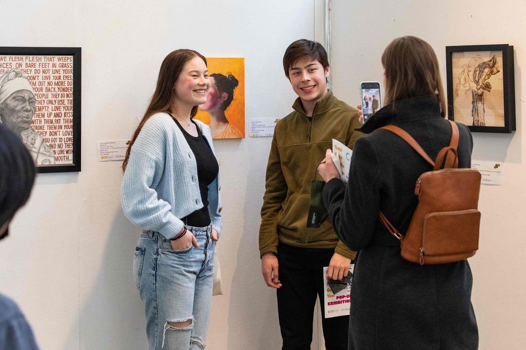 Two students pose for a photo in front of a painting.