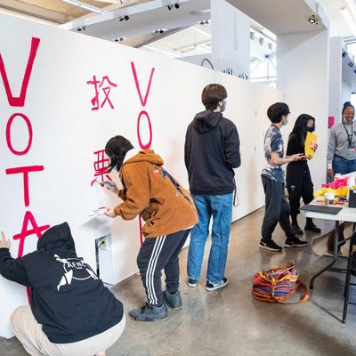 Students painting “vote” on a white wall, working together to amplify voting efforts.