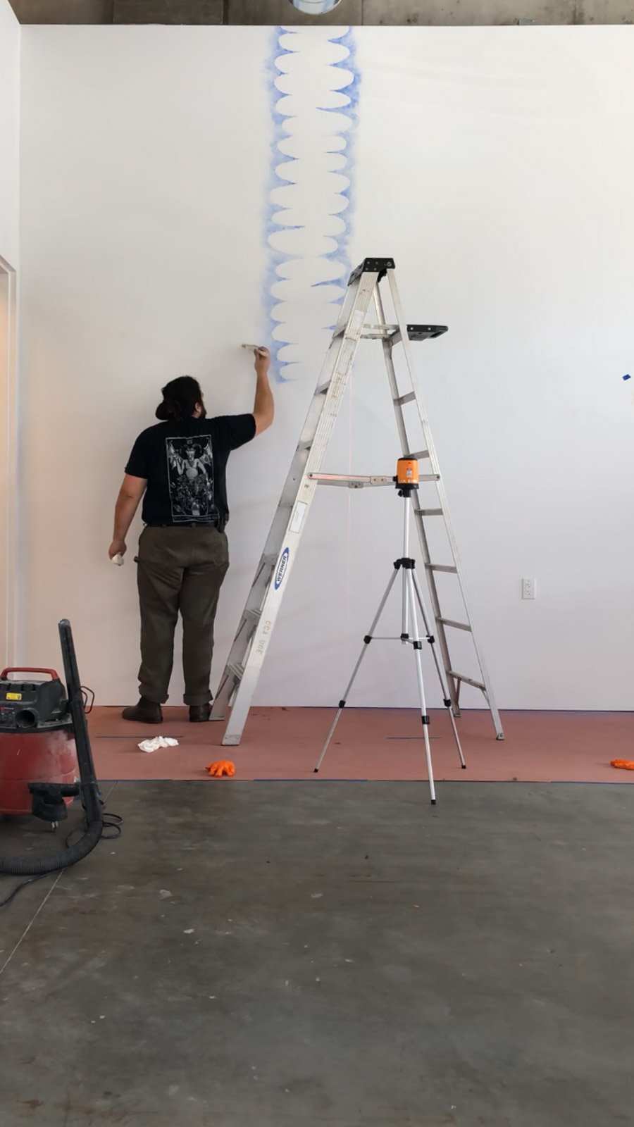 Photo of the artist installing their work on the walls of a gallery.