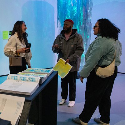 A group of visitors mingle with posters in hand at the opening of the Studio Forward exhibition.