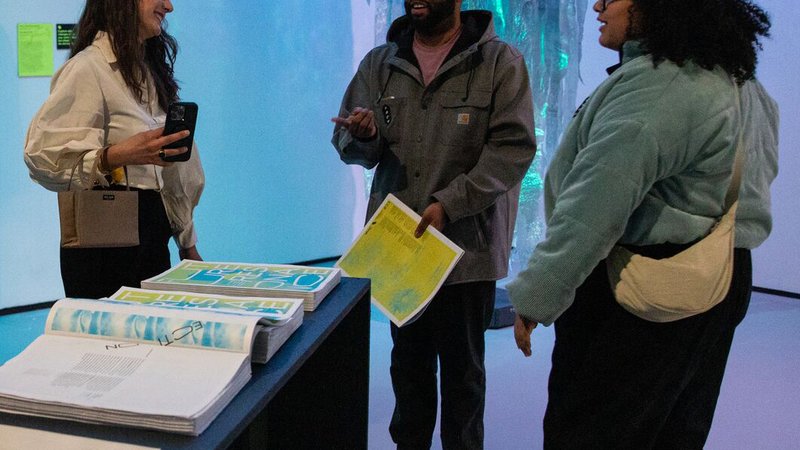 A group of visitors mingle with posters in hand at the opening of the Studio Forward exhibition.