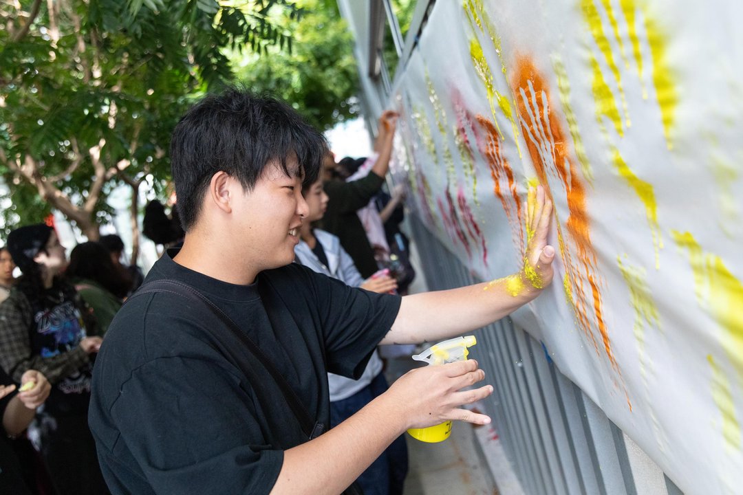 A group of students creating artwork by pressing painted hands onto a large vertical canvas.