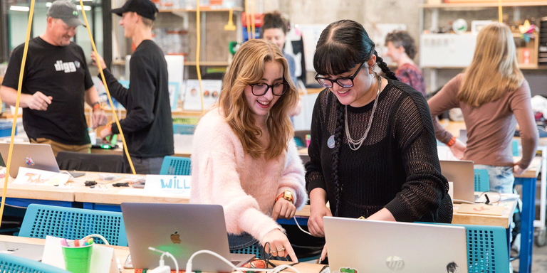 Two female students in a classroom playing with wearable technology