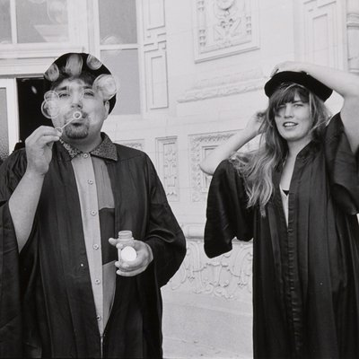 Two students in tams and gowns blow bubbles at the camera.