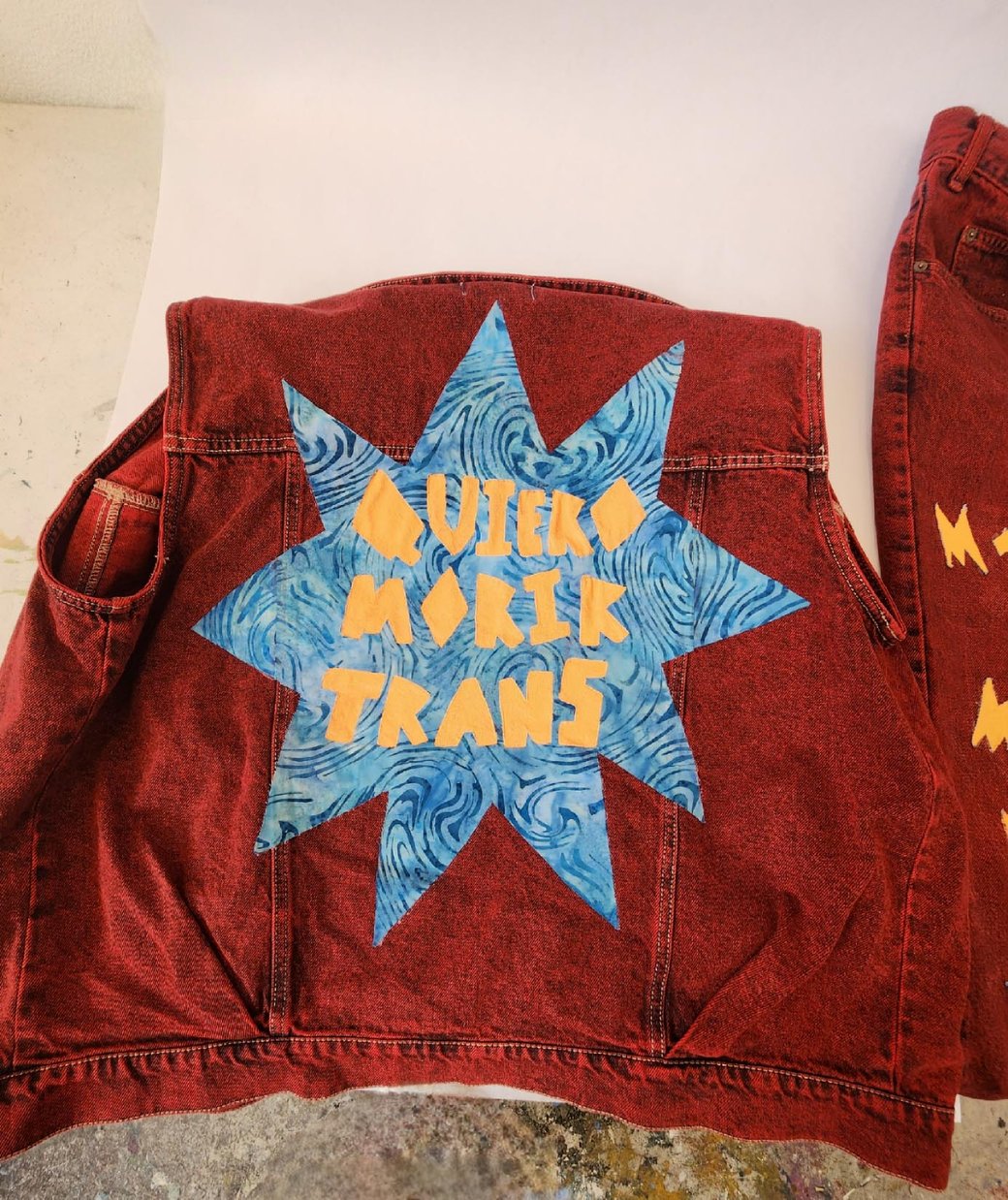 A photo of the back of a red vest with the Spanish text “Quiero morir trans.”