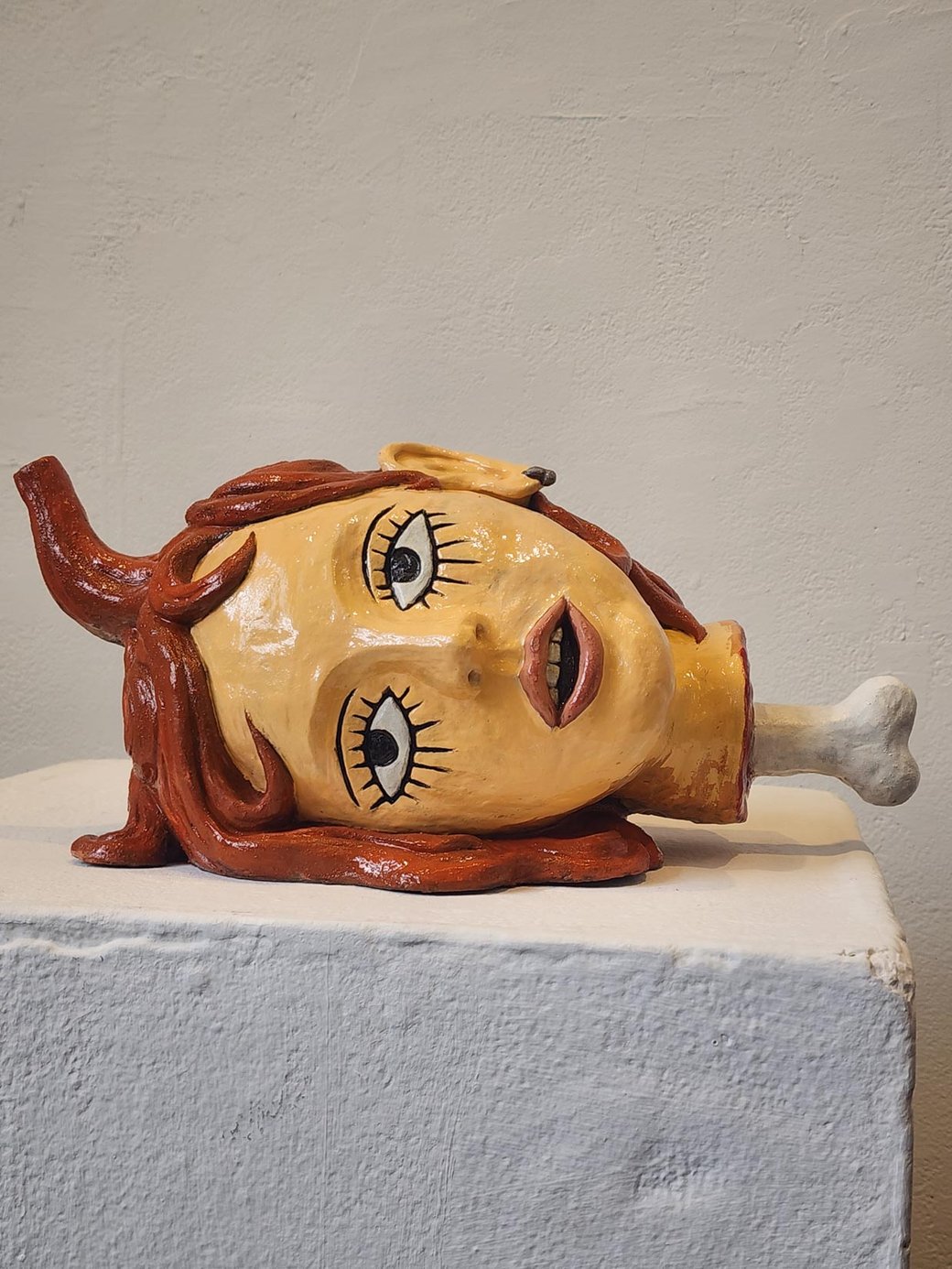A photo of a sculpture of the bust of a woman with her head down sideways and a bone protruding from the neck