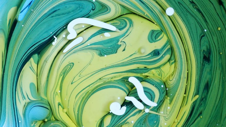 Close-up of abstract swirls in green and yellow hues with scattered white splotches, resembling paint mixing.