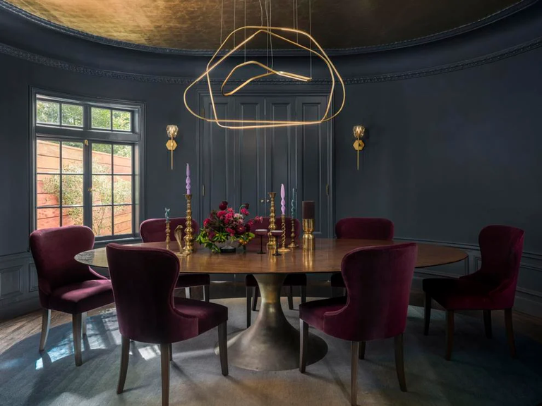 In the oval dining room nests a Julian Chichester table, custom Black Label Home chairs in Schumacher velvet and a custom rug by Ombre. The walls are painted Farrow and Ball’s Hague Blue, while the chandelier by Galerie Philia descends from a gold leaf painted ceiling by David Bonk.